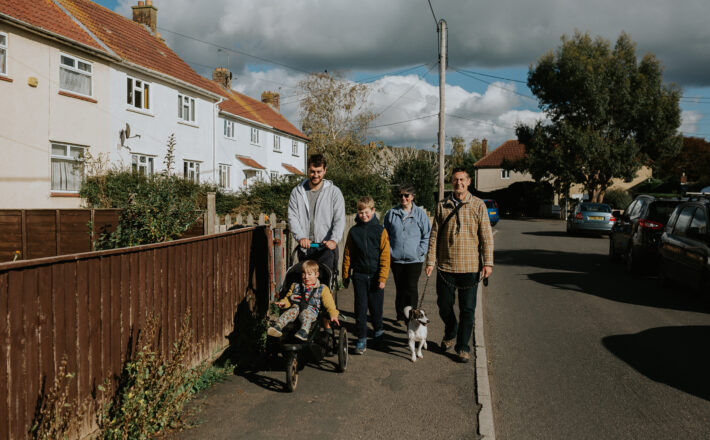 Family walking in a village through affordable housing by Abigail Oliver